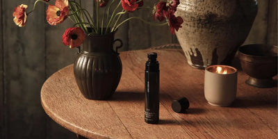 Essential oils for cleaning featured in a Homecourt room deodorant beside a candle and wildflowers on a wood table.