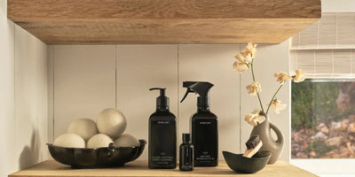 How to reduce toxins in your home with stylish black bottles of natural laundry and linen care products on wooden shelves.
