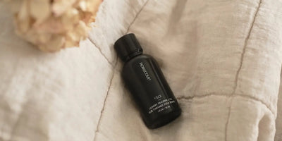 Laundry fragrance oil bottle resting on a soft beige quilt for a cozy, elevated laundry experience.