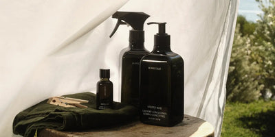 Plant-based laundry detergent set with linen spray and fragrance oil on a wooden surface with sunlight and greenery.