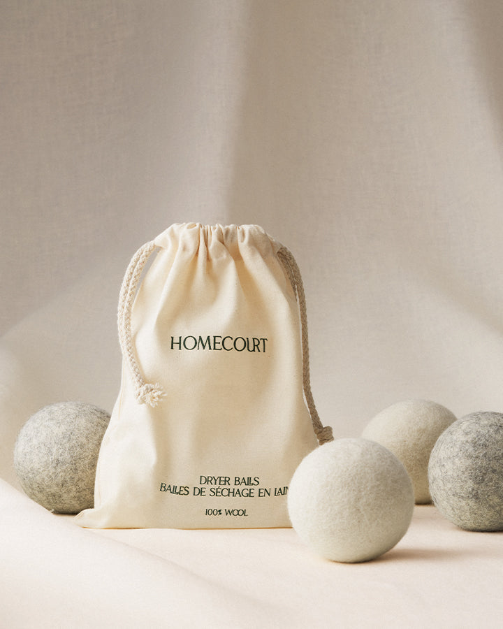 Front view of wool dryer balls set showing drawstring storage bag and four balls, two natural and two gray, on a neutral backdrop