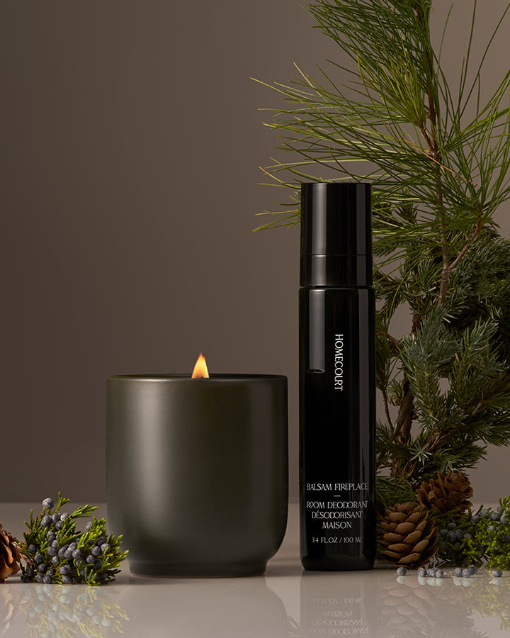Front view of Aircare Duo showing black deodorant spray and lit green candle with pine sprigs on brown background