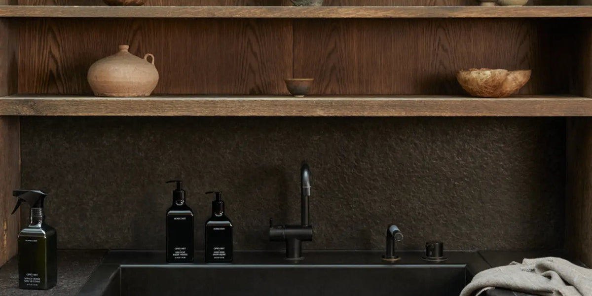Homecourt Cipres Mint dish soap, hand wash and surface cleaner on a black stone sink ledge under oak shelves holding clay pots