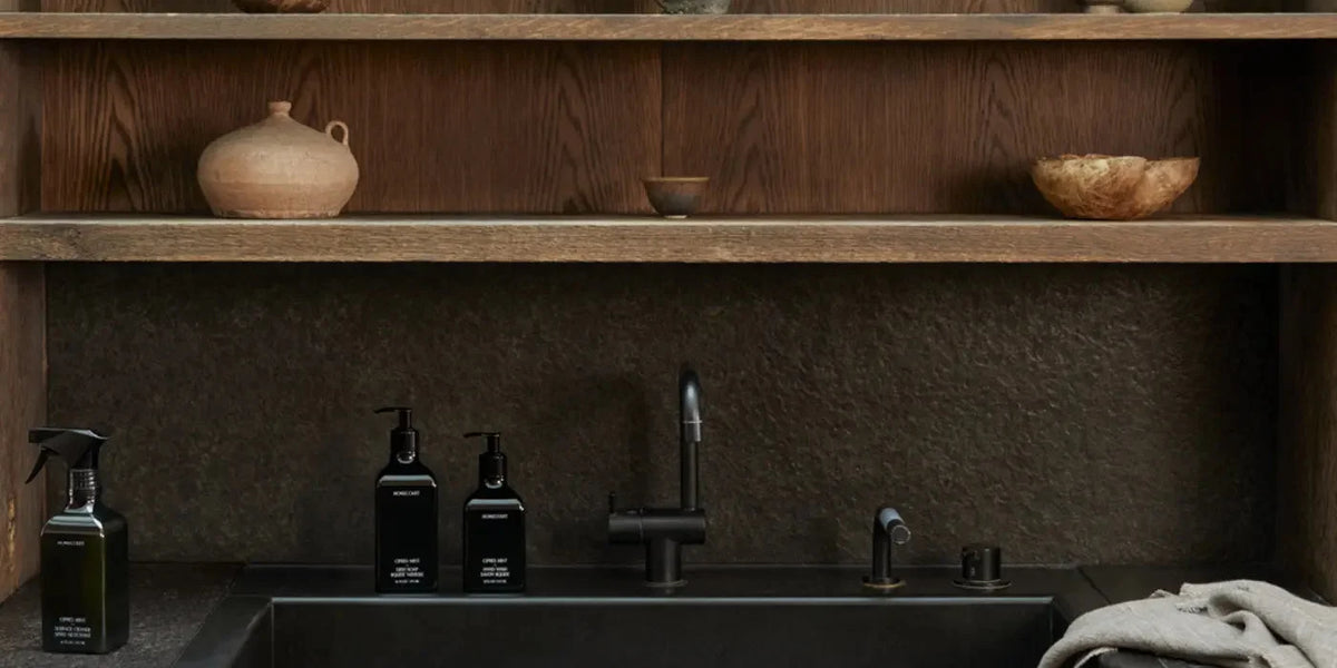 Homecourt Surface Cleaner, Dish Soap and Hand Wash in Cipres Mint beside a matte black faucet and sink, under oak shelves holding stoneware pots