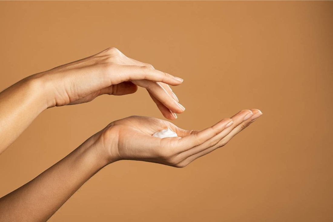 Hands applying a dollop of hand cream against a warm beige background
