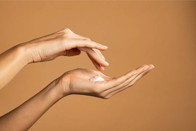 Hands applying a dollop of hand cream against a warm beige background