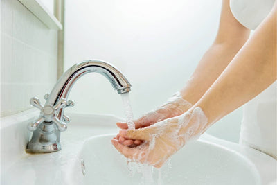 Person washing soapy hands under a chrome bathroom faucet