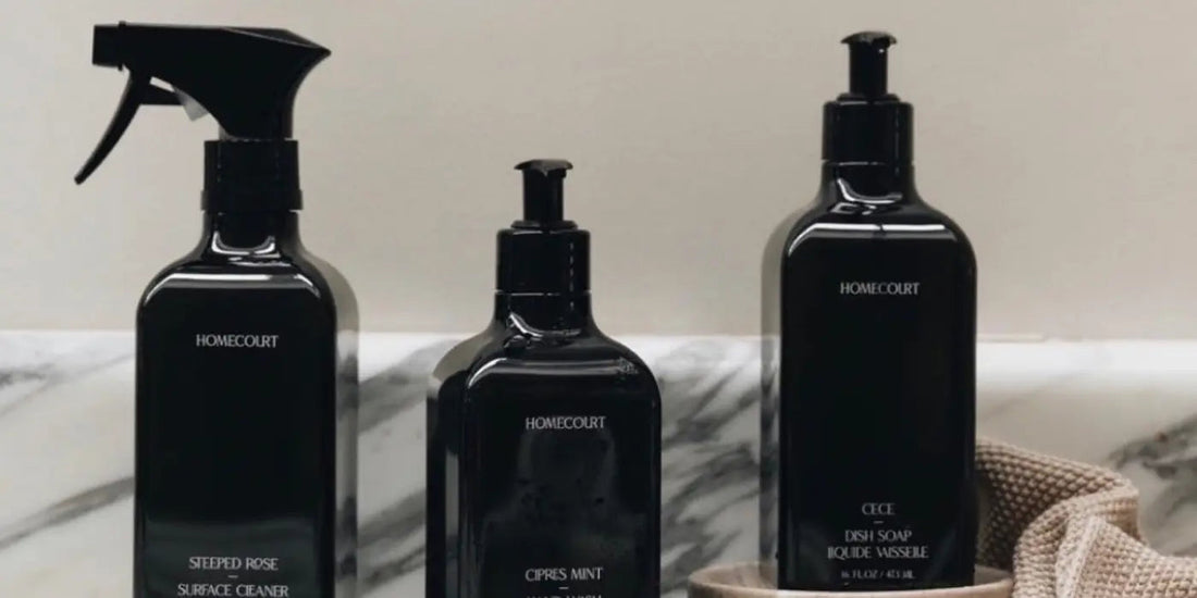 Front view of three Homecourt cleaning bottles (dish soap and surface cleaner) with black pumps on a marble counter