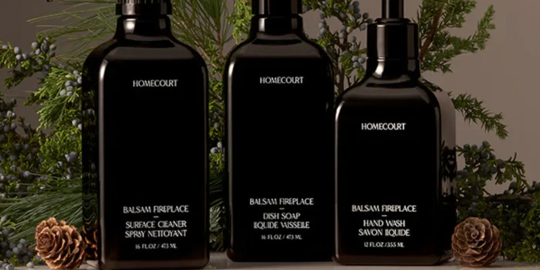 Front view of three black Homecourt bottles (dish soap, hand wash, surface cleaner) with evergreen sprigs and pine cones
