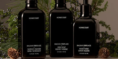 Front view of three black Homecourt bottles (dish soap, hand wash, surface cleaner) with evergreen sprigs and pine cones