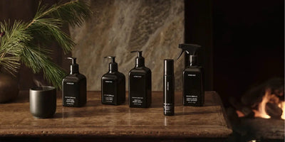 Front view of Homecourt black hand and home-care bottles with pump dispensers on a wooden table by a fireplace