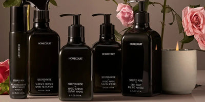 Front view of Homecourt Steeped Rose dish soap, hand wash, and hand cream in black bottles with roses and lit candle