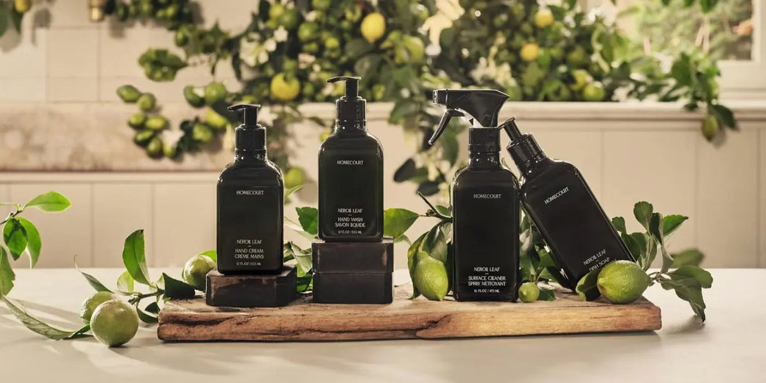 Front view of Homecourt Neroli Leaf cleaning bottles, black pump and spray, on a wood board with citrus and leaves