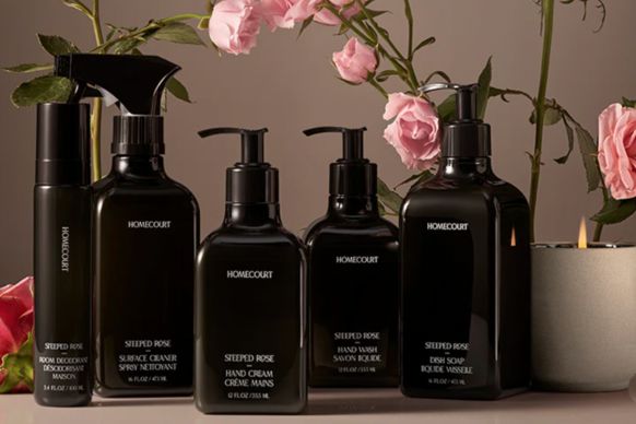 Front view of Homecourt Steeped Rose cleaning and hand care bottles showing black pump bottles with pink roses and candle background