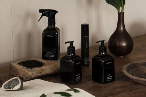 Three-quarter view of black refillable cleaning bottles showcasing pump and spray dispensers on a wooden table with a vase and open book in soft natural light