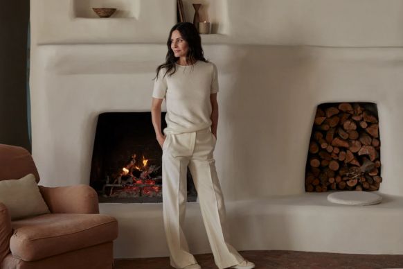 Woman standing by a lit plaster fireplace in a neutral-toned living room