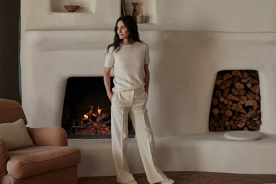 Woman standing by a lit plaster fireplace in a neutral-toned living room