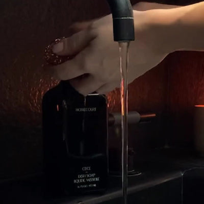 Front view of Homecourt Cece dish soap bottle showcasing pump dispenser next to a running faucet on a dark countertop