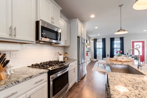 Open-plan kitchen showing stainless steel stove and refrigerator, granite countertops and island with sink