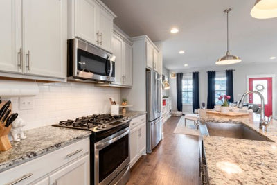 Open-plan kitchen showing stainless steel stove and refrigerator, granite countertops and island with sink