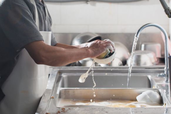 Person washing soapy dishes at a stainless steel sink with a running faucet