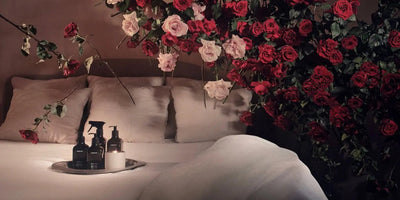 Bottles of hand-care products on a silver tray on a bed with pillows and hanging red and pink roses creating a spa-like setting