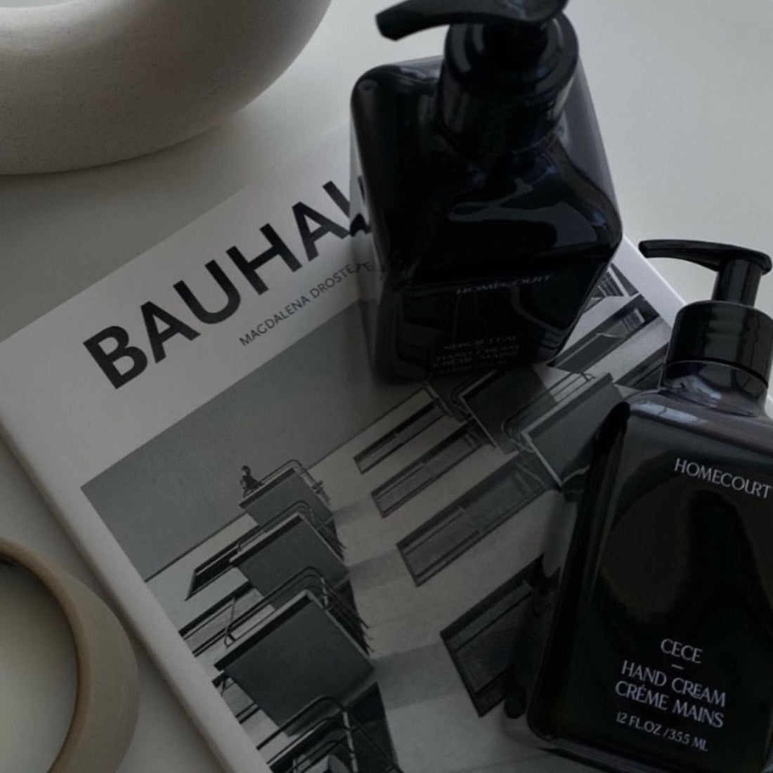 Top-down view of two CECE hand cream pump bottles showing pump dispensers on a Bauhaus book