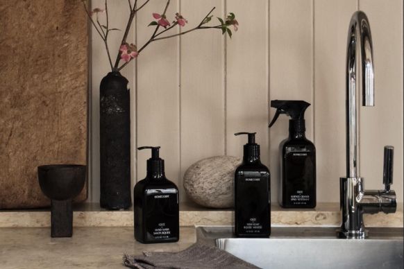 Three black dish soap bottles arranged by a kitchen sink with a chrome faucet, stone countertop, and decorative vase