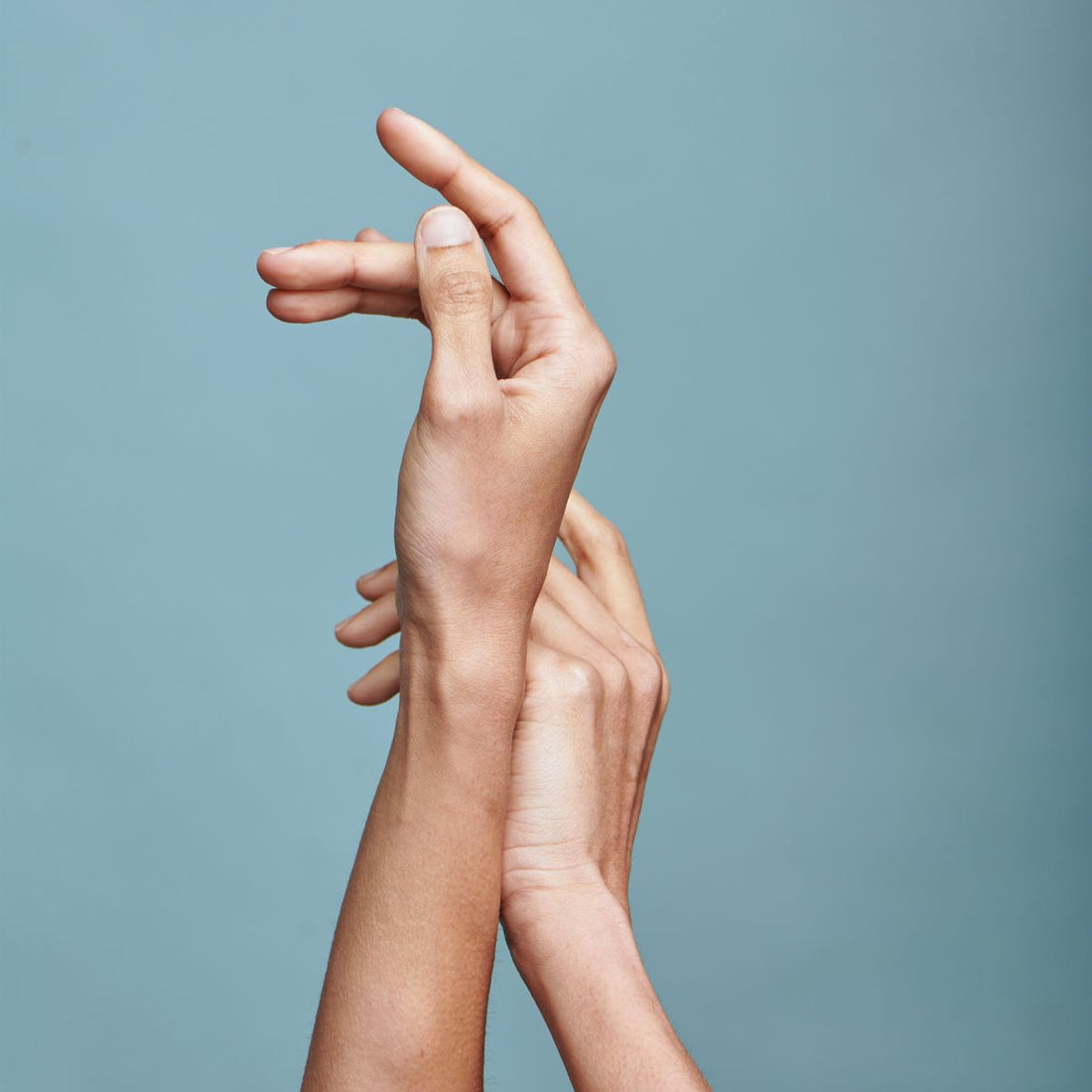 Close-up of two hands gently touching against a pale blue background