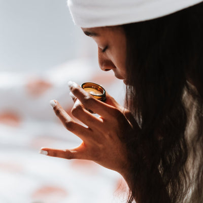 Woman smelling a small amber jar candle in a sunlit bedroom