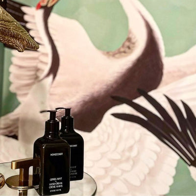 Front view of two Homecourt hand cream pump bottles on a mirrored tray with swan mural background