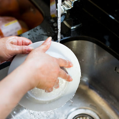 Hands washing a white plate under running tap water in a kitchen sink