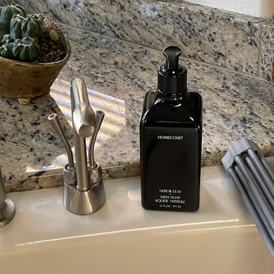 Front view of black Homecourt Neroli Leaf dish soap bottle with pump on granite sink countertop beside stainless faucet