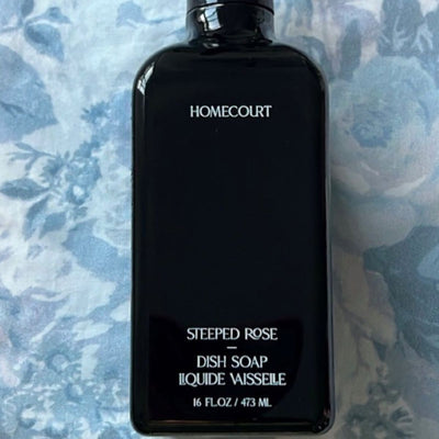 Top-down view of Homecourt Steeped Rose dish soap, black bottle with white label text on blue floral background