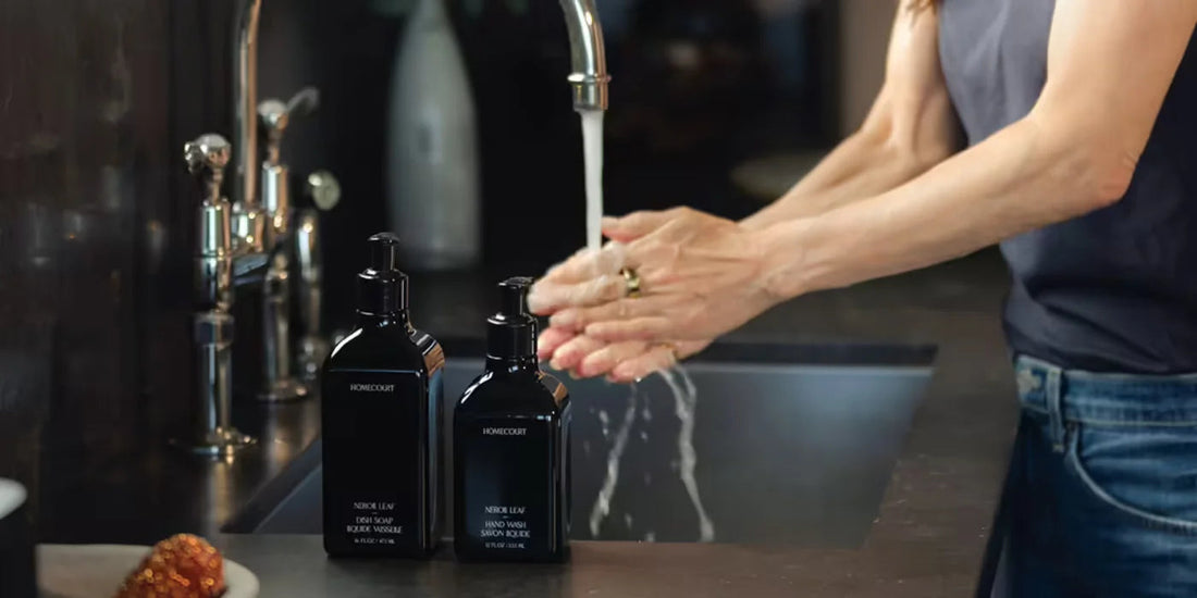Person washing hands at a kitchen sink beside two black Homecourt soap pump bottles on the counter