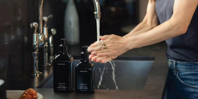 Person washing hands at a kitchen sink beside two black Homecourt soap pump bottles on the counter