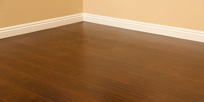 Corner of an empty room with glossy dark brown laminate flooring, cream baseboards and beige walls