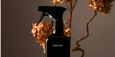 Front view of black Homecourt spray bottle showcasing trigger sprayer and minimalist label with dried hydrangea stems against a warm brown backdrop