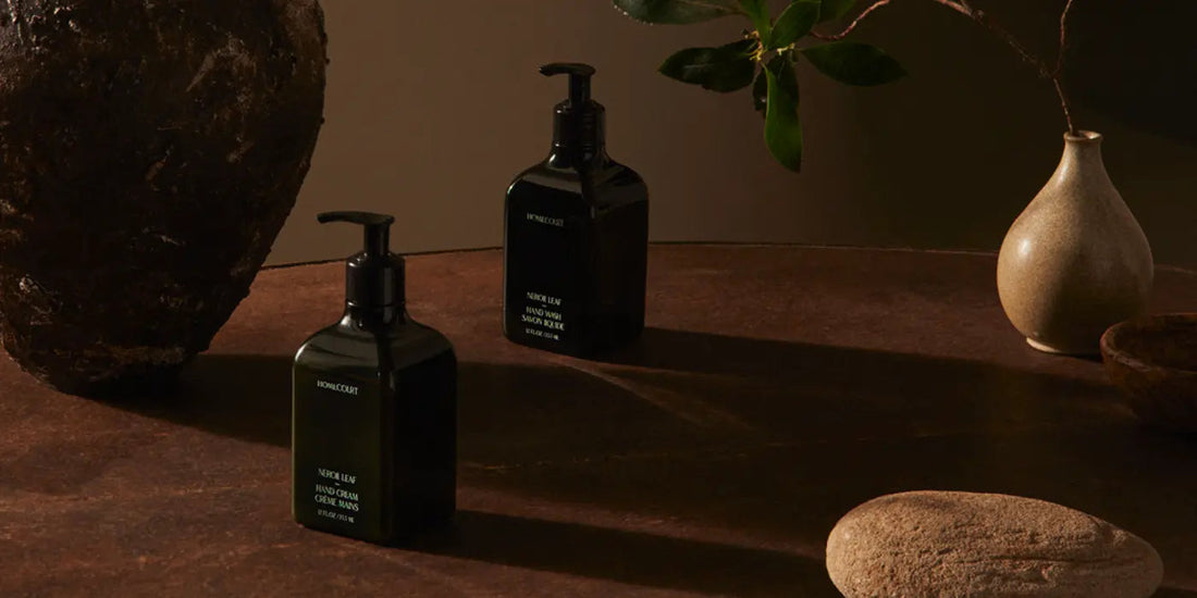 Front view of two dark glass hand wash bottles showcasing pump dispensers and minimalist labels on a brown stone tabletop