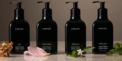 Front view of four Homecourt hand cream pump bottles showing black rectangular bottles with floral accents on a neutral background