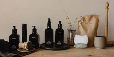 Homecourt cleaning bottles and refill pouch arranged on a wooden table with brushes, sponge, and vase against a neutral wall