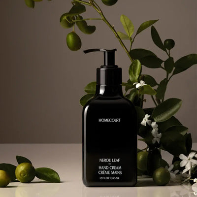 Front view of Homecourt Neroli Leaf hand cream pump bottle, glossy black with neroli branches on soft brown background