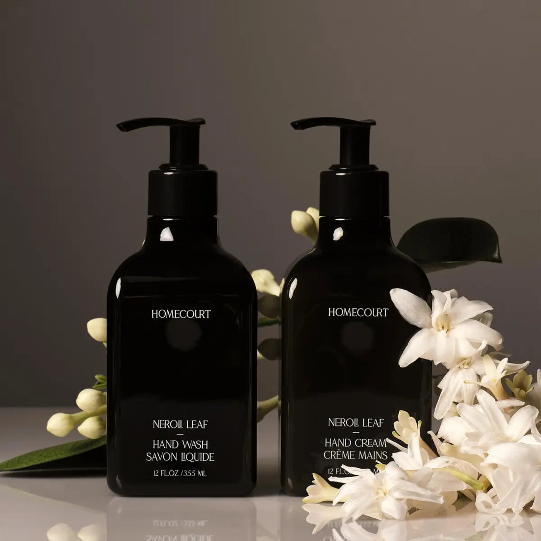 Front view of two Homecourt Neroli Leaf pump bottles, hand wash and hand cream, glossy black with white flowers