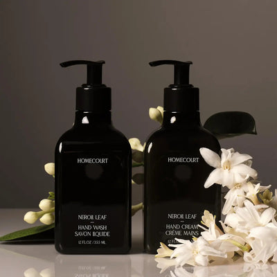 Front view of two Homecourt Neroli Leaf pump bottles, hand wash and hand cream, glossy black with white flowers