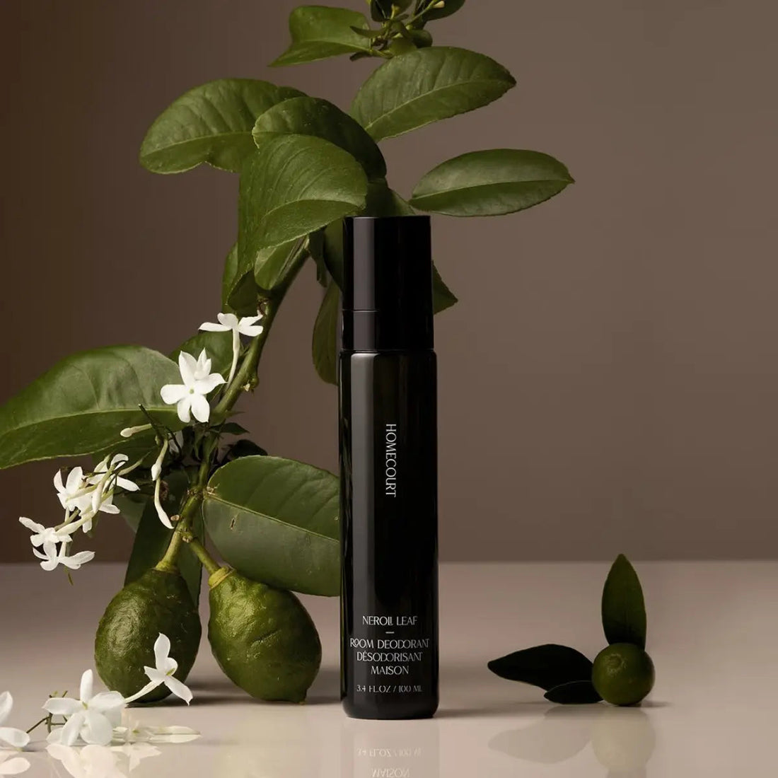 Front view of Homecourt Neroli Leaf room deodorant: black 3.4 fl oz spray bottle with citrus leaves and jasmine flowers