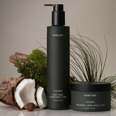 Front view of Homecourt COCOMOI body wash pump and body butter jar in dark green packaging with halved coconut and driftwood