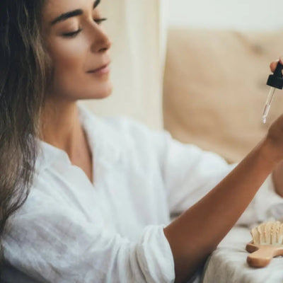 Woman applying perfume oil with a dropper to her wrist while seated on a sofa