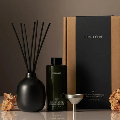 Front view of CECE reed diffuser set showing matte black vase with reeds, dark green HOMECOURT oil bottle, metal funnel and kraft box on brown background