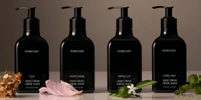 Front view of four Homecourt black pump hand creams labeled with different scents, arranged with flowers and citrus