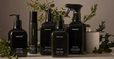 Front view of Homecourt Cipres Mint dish soap and matching home care bottles on counter with greenery and lit candle